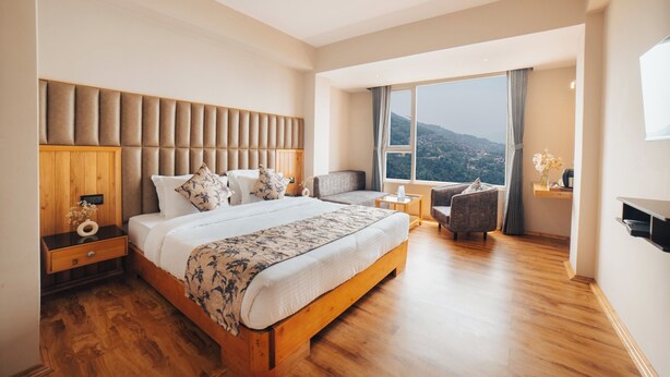 Ein geräumiges Schlafzimmer mit einem großen Bett, einem Holzkopfende, Blick auf die Berge durch ein großes Fenster und einer kleinen Sitzecke mit einem Sessel und einem Beistelltisch.