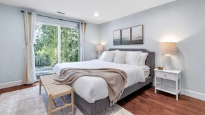 Ein Schlafzimmer mit Bett, Nachttischen, einer Bank und Blick auf Grünfläche.
