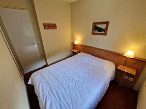 Una cama individual con cabecera de madera, dos lámparas de noche, un pequeño estante de madera y un cuadro enmarcado en la pared.