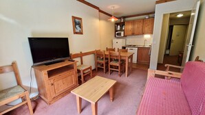 Ein kompakter Wohnraum mit Fernseher, Holzmöbeln, einer Küchenzeile und einem roten Sofa.