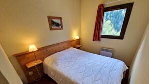 Ein Schlafzimmer mit einem hölzernen Kopfteil, einem Einzelbett mit weißer Bettdecke, einem Nachttisch mit Lampe, einem Wandbild und einem Fenster mit Vorhängen.