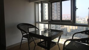 A balcony with a table and chairs, overlooking a cityscape with buildings and a bridge. - Kaixuan Shidai Family Apartment (Dalian)