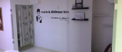 A bedroom with a bed, a wall with a quote, a door with curtains, and a shelf with pictures.