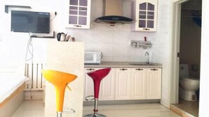 A compact kitchen with a microwave, stove, and a TV mounted on the wall. - Kaixuan Shidai Family Apartment (Dalian)