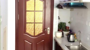 A kitchen with a wooden door, a stainless steel sink, and various potted plants. - Kaixuan Shidai Family Apartment (Dalian)