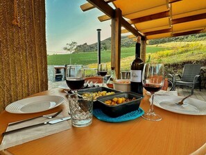 A table set for two with wine glasses, a bottle of wine, and a dish of food, overlooking a scenic landscape. - Nature Lovers Cabin- Hottub- Privacy & Serenity (Montecorto)