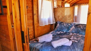 Una habitación de cabaña de madera con una cama, cortinas de encaje y un cabecero tejido.