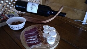 Una botella de vino, un bol de frutos secos y un plato con lonchas de carne y queso sobre una mesa de madera.