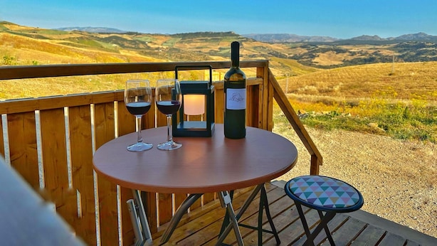 Una terraza de madera con una mesa, dos copas de vino, una botella y un farol.