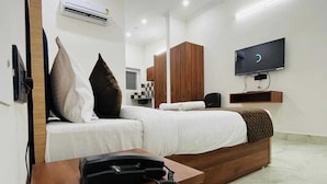Una habitación de hotel moderna con cama, escritorio con teléfono, ventilador de techo, equipo de aire acondicionado, televisión y baño con espejo y armario.