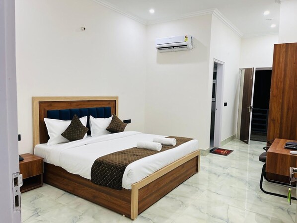Una habitación de hotel con una cama de madera, ropa de cama blanca, piso de mármol, un equipo de aire acondicionado y un armario de madera.