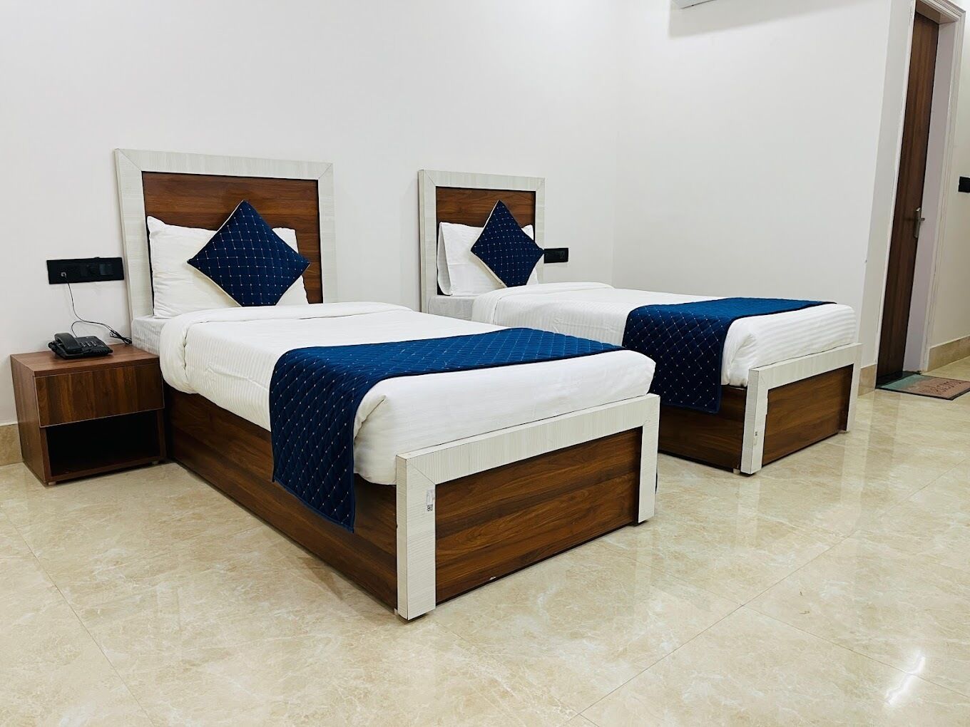 Une chambre d’hôtel avec deux lits, chacun doté d’une tête de lit en bois, de draps blancs et de couvertures bleues. Il y a une table de chevet sur laquelle se trouve un téléphone.