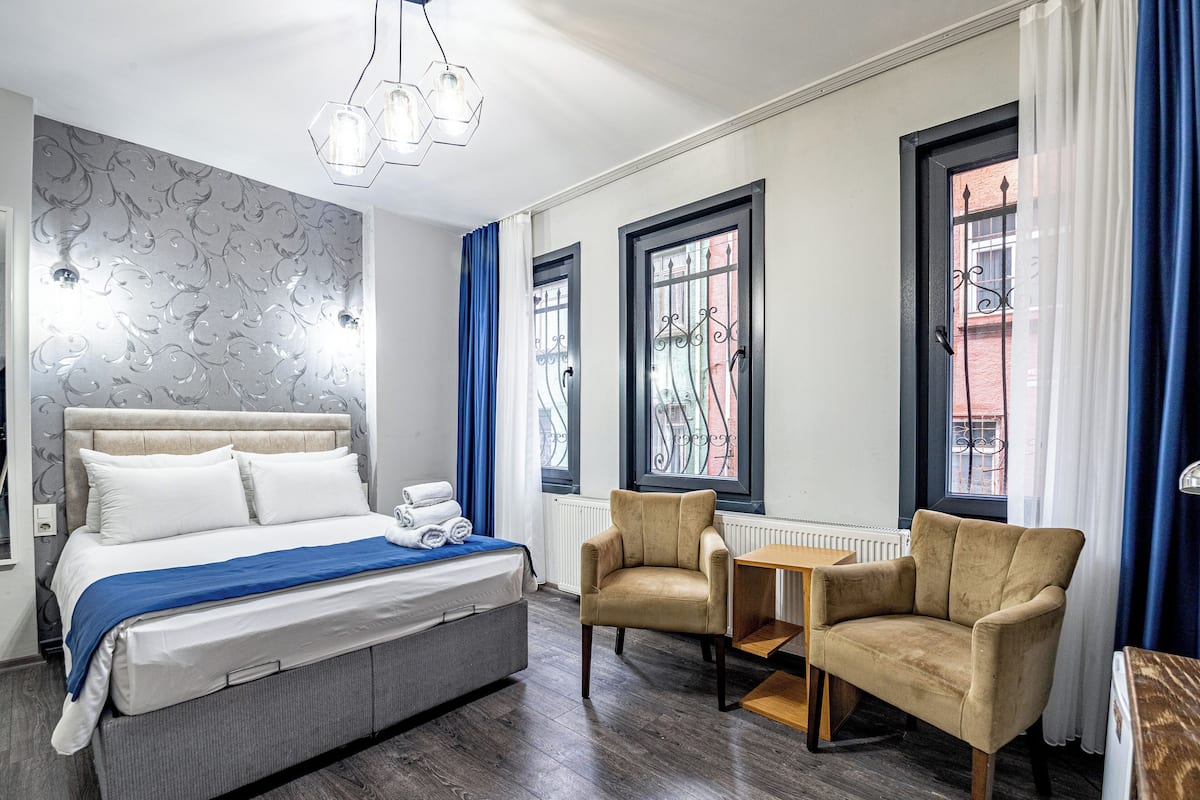 A hotel room with a bed, two armchairs, a small table, and a window with curtains.