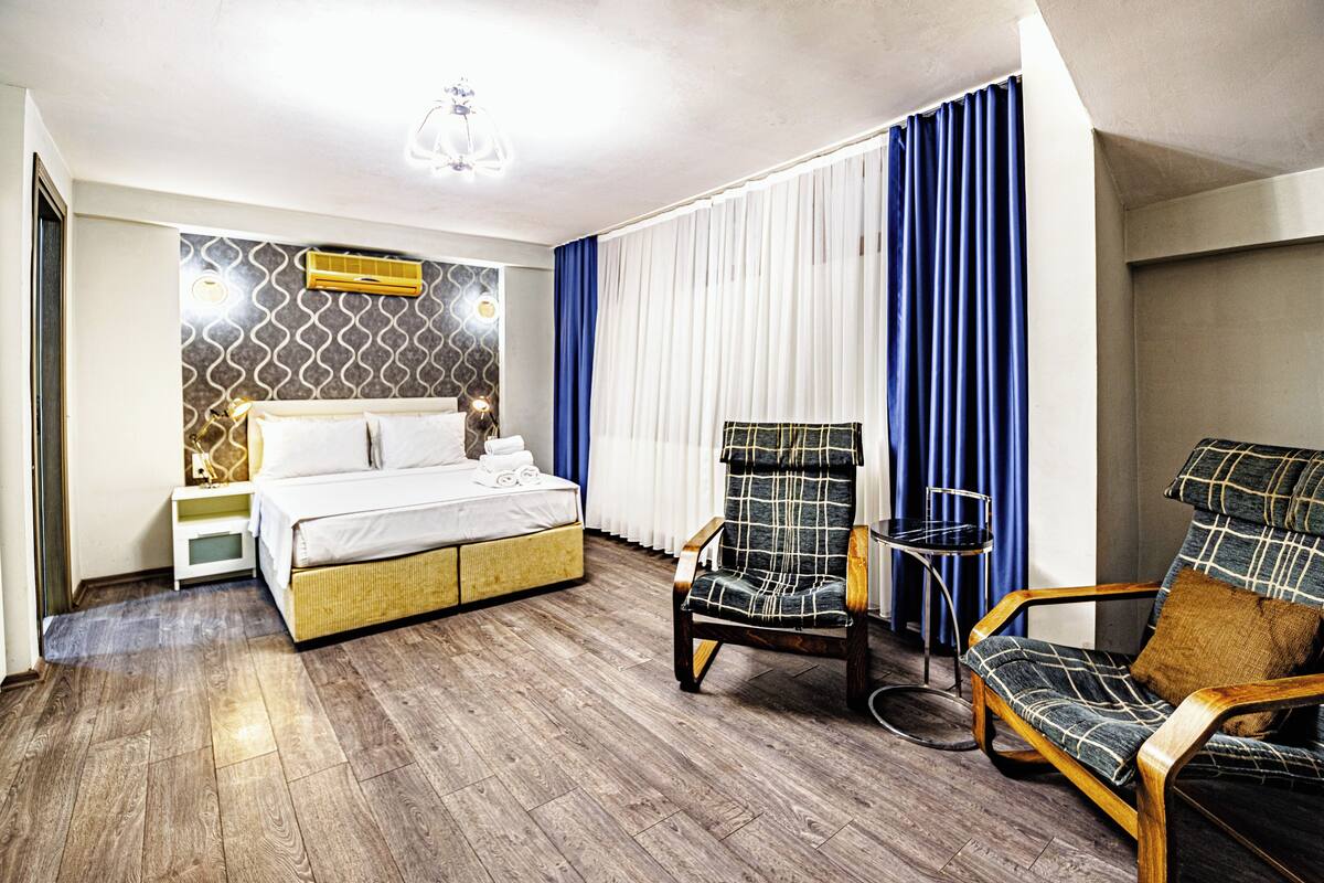 A hotel room with a bed, two armchairs, a small table, and a wall-mounted air conditioner.