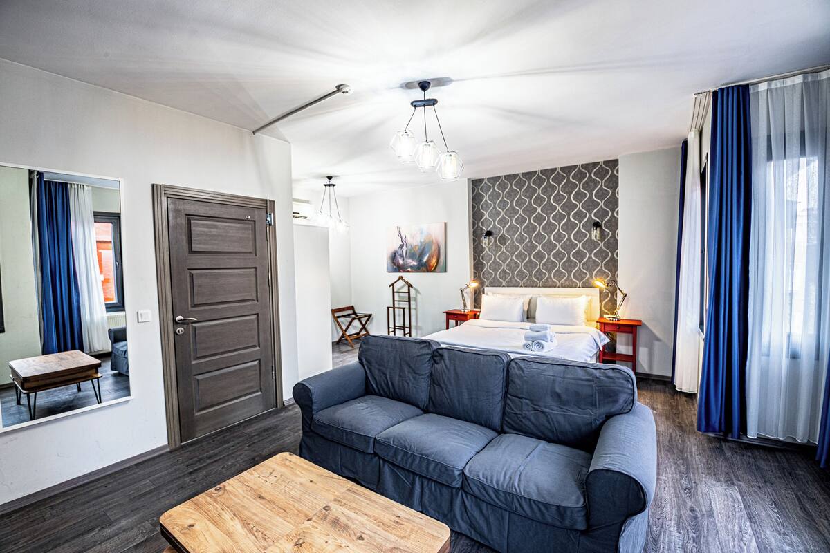 A modern hotel room with a grey sofa, a wooden coffee table, a bed with white linens, and a patterned wall.