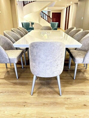 Un espace repas moderne avec une grande table rectangulaire entourée de chaises grises à revêtement en tissu et à pieds métalliques.