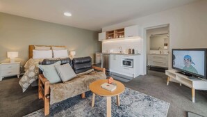 A modern bedroom with a bed, a sofa, a small round table, a TV, and a kitchenette. - Starry Slumber - Your Cozy Retreat in Lake Tekapo (Lake Tekapo)