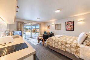 A hotel room with a bed, a desk with a computer, a chair, and a view through a glass door to the outdoors. - Starry Slumber in Lake Tekapo | Views & Parking (Lake Tekapo)