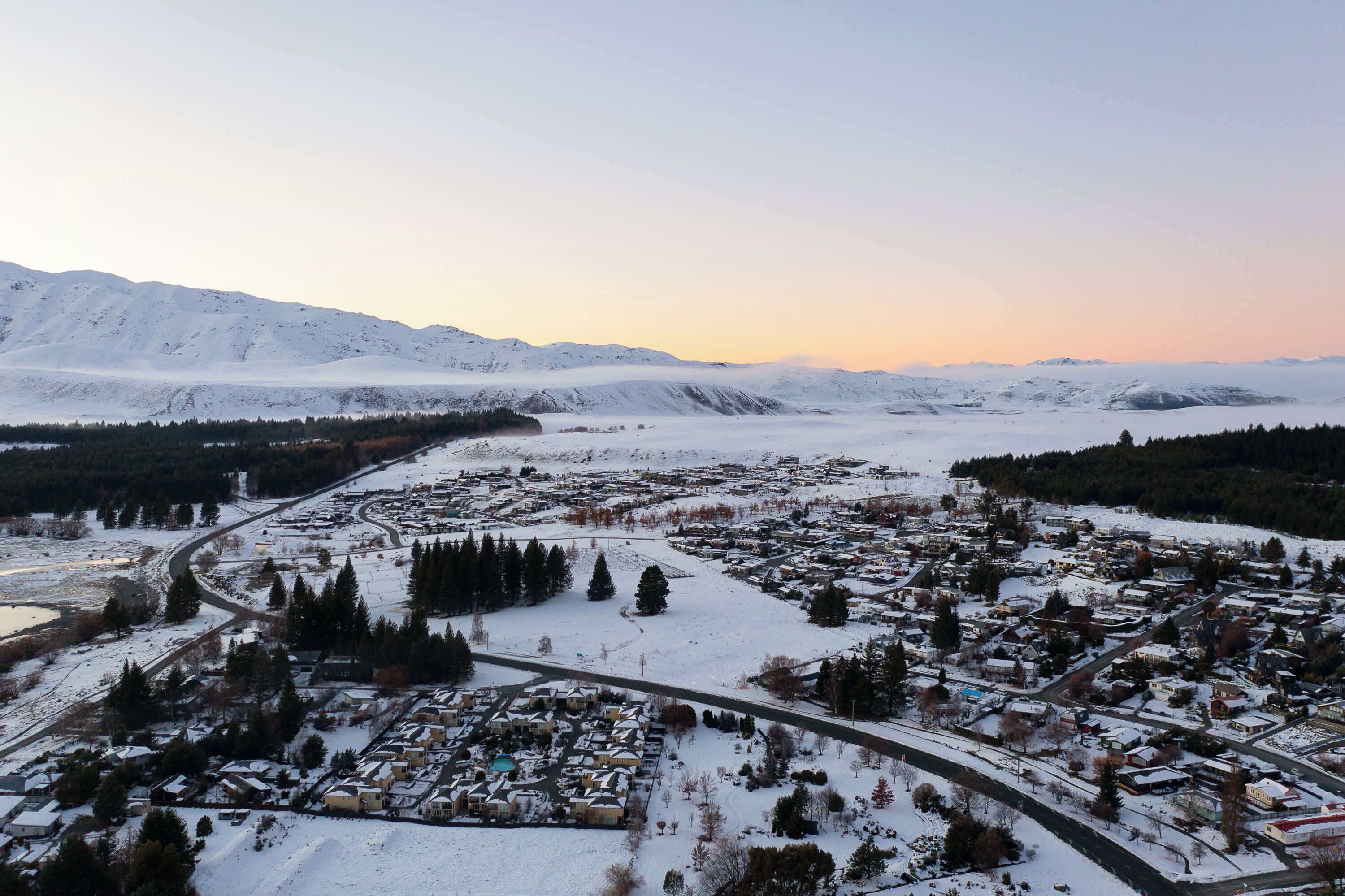 A snow-covered town with a river running through it, surrounded by mountains.