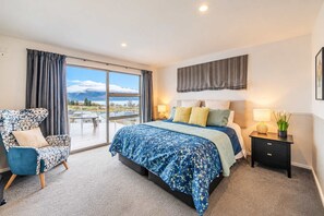 Een slaapkamer met een groot bed, een stoel, een nachtkastje en uitzicht op het groen.