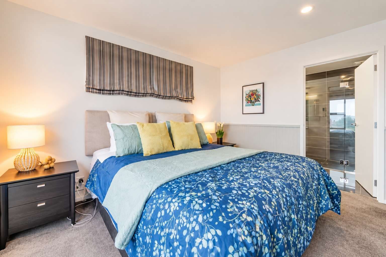 A bedroom with a bed, bedside tables, a wall-mounted artwork, and a door leading to a bathroom.
