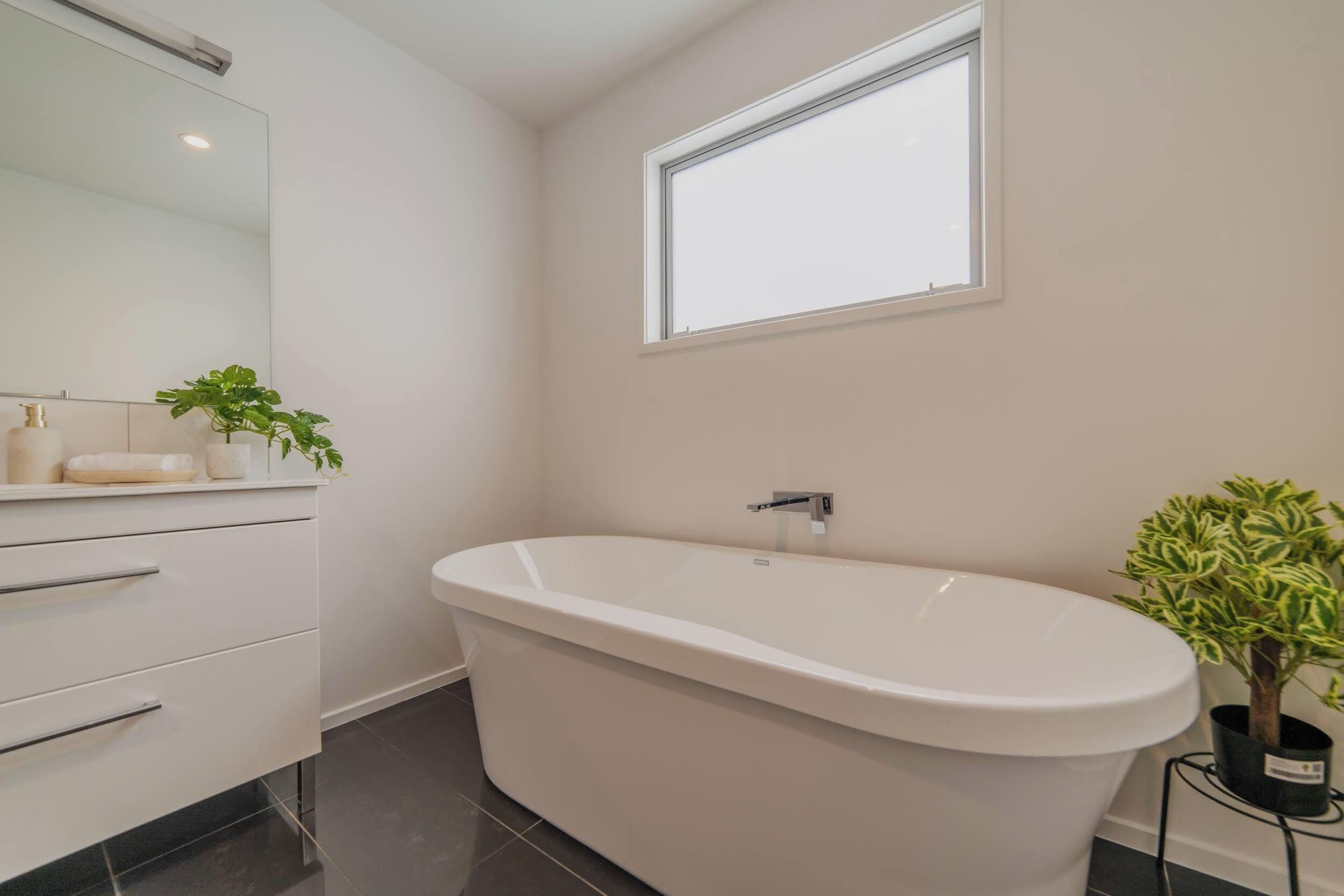 A modern bathroom with a freestanding bathtub, a large mirror, and a window.