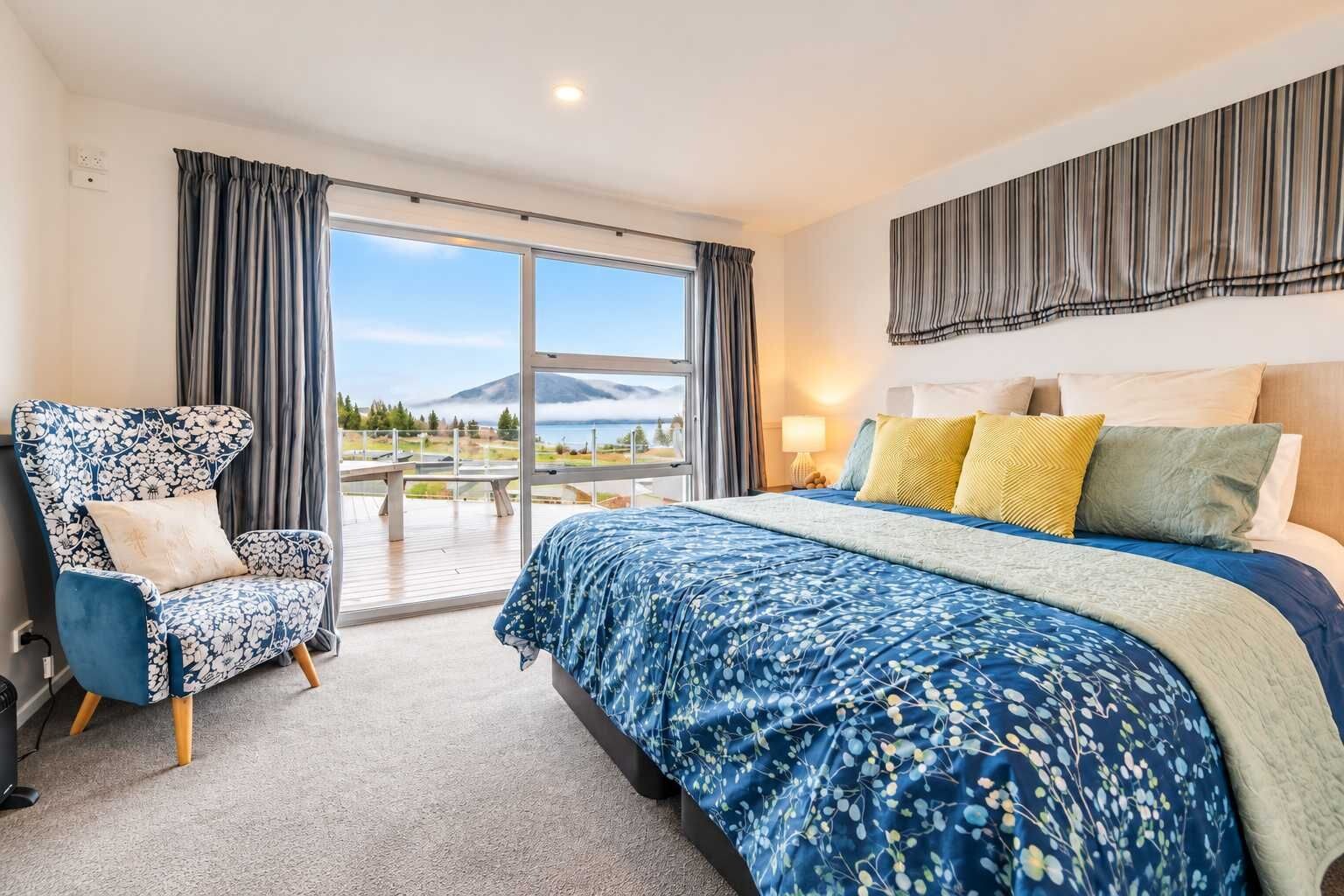 A hotel room with a large bed, a chair, a view of a mountain, and a balcony.