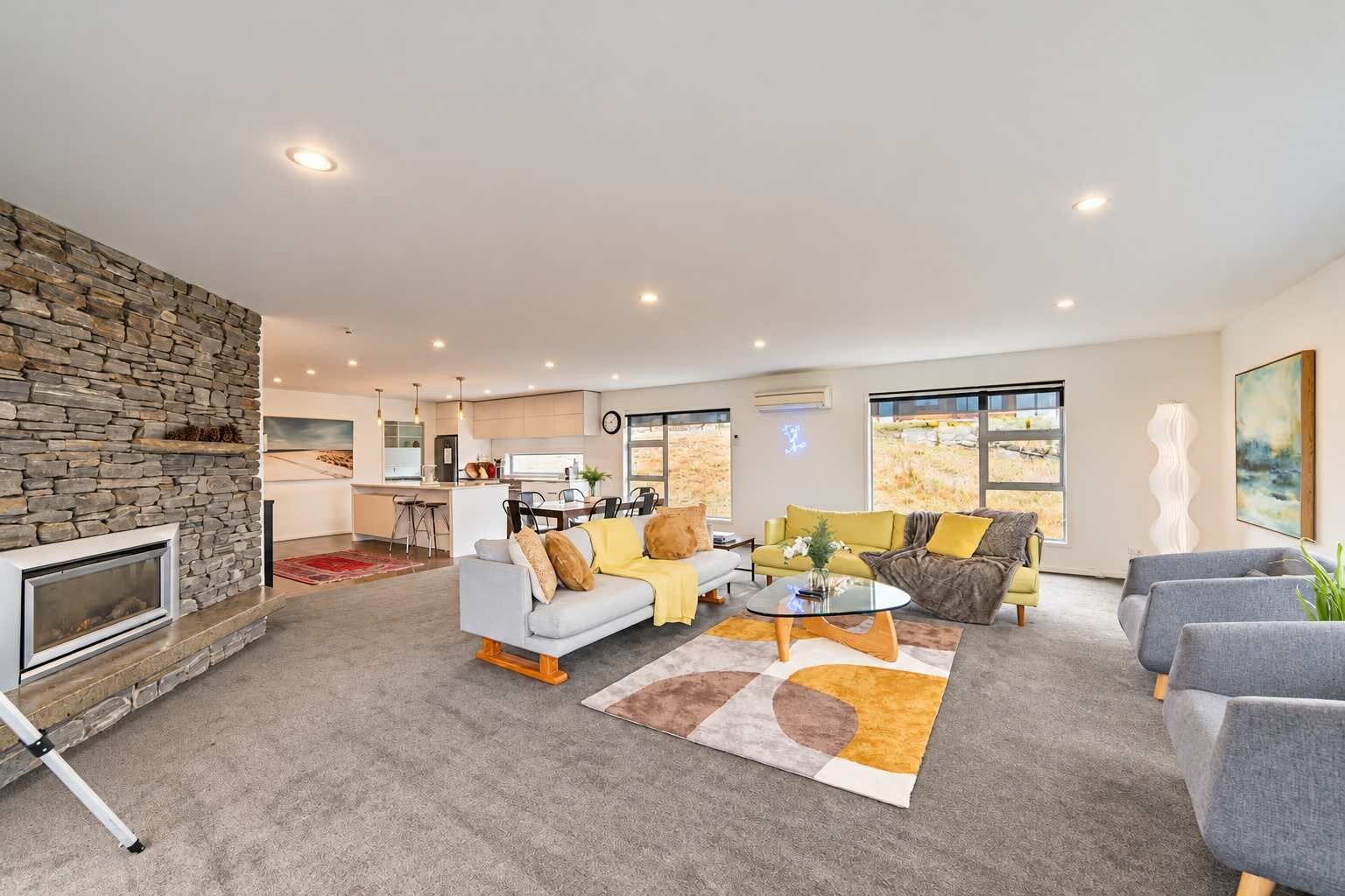 A spacious living area with a stone fireplace, a dining area, and a view of a field through large windows.