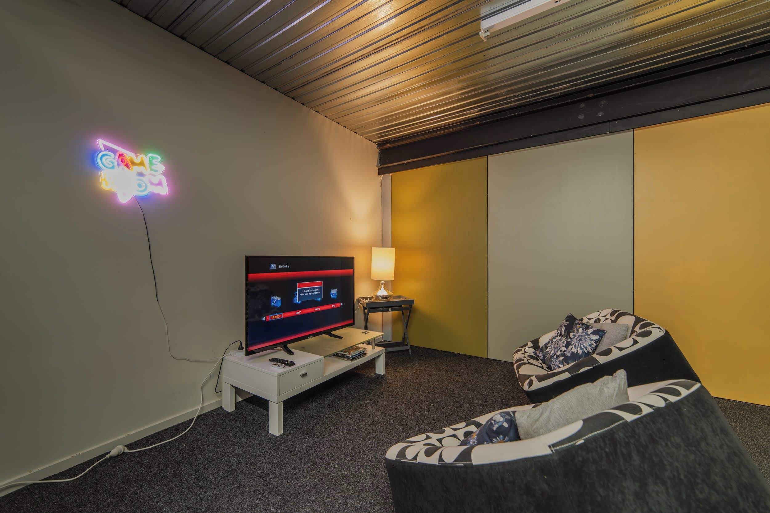 A modern hotel room with a flat-screen TV, a neon sign, a lamp, and a sofa.