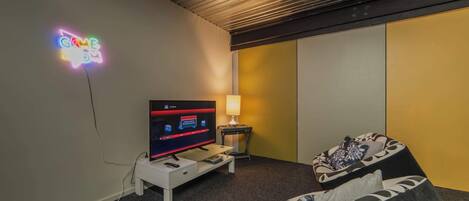 A modern hotel room with a flat-screen TV, a neon sign, a lamp, and a sofa.