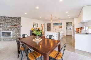 A modern kitchen with a central island, a dining area with a wooden table and chairs, and a stone fireplace. - Hillside Haven | Tekapo | 3BR with Games & Views (Lake Tekapo)