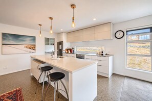 A modern kitchen with a central island, bar stools, pendant lighting, and a view through the window.