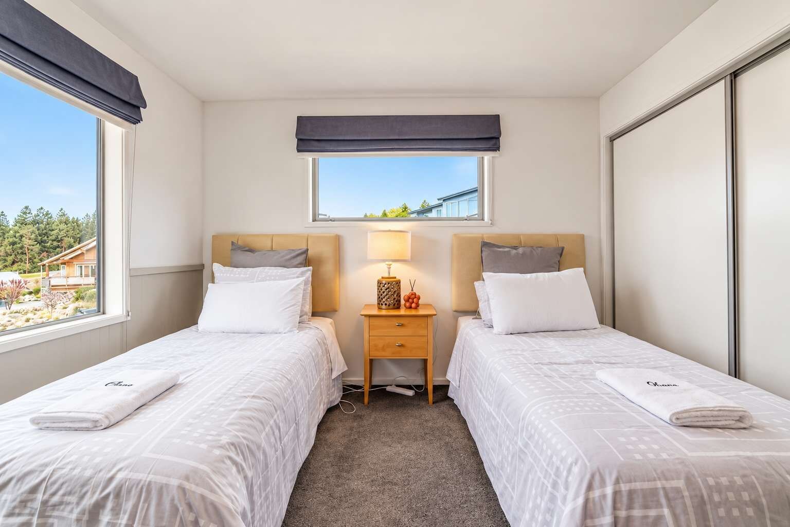 A hotel room with two beds, a nightstand with a lamp, a window with a view, and a small table with a decorative item.