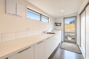 A modern kitchen with white cabinetry, a stainless steel sink, and a window overlooking a landscape. - Hillside Haven | Tekapo | 3BR with Games & Views (Lake Tekapo)