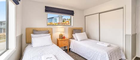 A hotel room with two beds, a window with a view, a bedside table with a lamp, and a wardrobe.