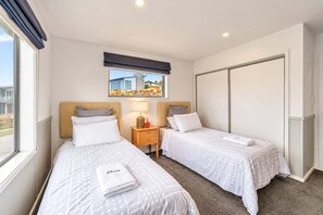 A hotel room with two beds, a window with a view, a bedside table with a lamp, and a wardrobe. - Hillside Haven | Tekapo | 3BR with Games & Views (Lake Tekapo)