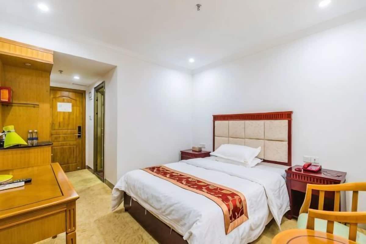 Ein Hotelzimmer mit Bett, Nachttisch, Stuhl, Schreibtisch, Lampe und einem Holzschrank.