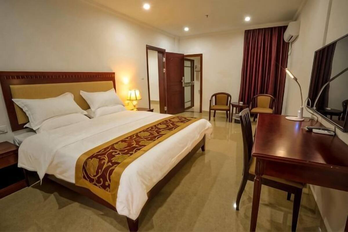 Ein Hotelzimmer mit Bett, Schreibtisch, Stuhl, Fernseher und einer Tür zu einem weiteren Raum.