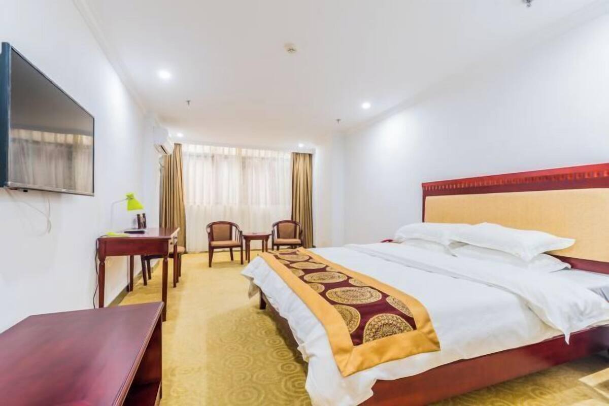 Ein Hotelzimmer mit Bett, Schreibtisch, zwei Stühlen, Fernseher und einem fensterbepflanzten Fenster.