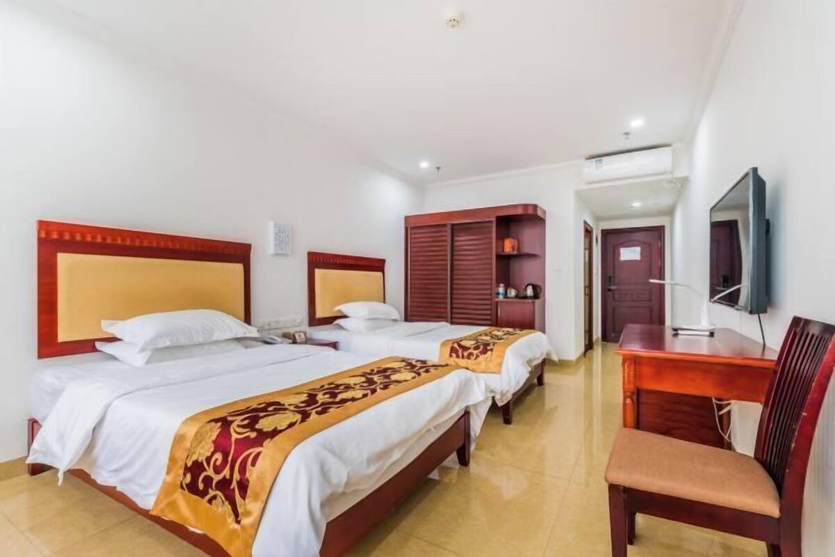 Ein Hotelzimmer mit zwei Betten, einem Schreibtisch, einem Stuhl, einem Fernseher und einem Kleiderschrank.