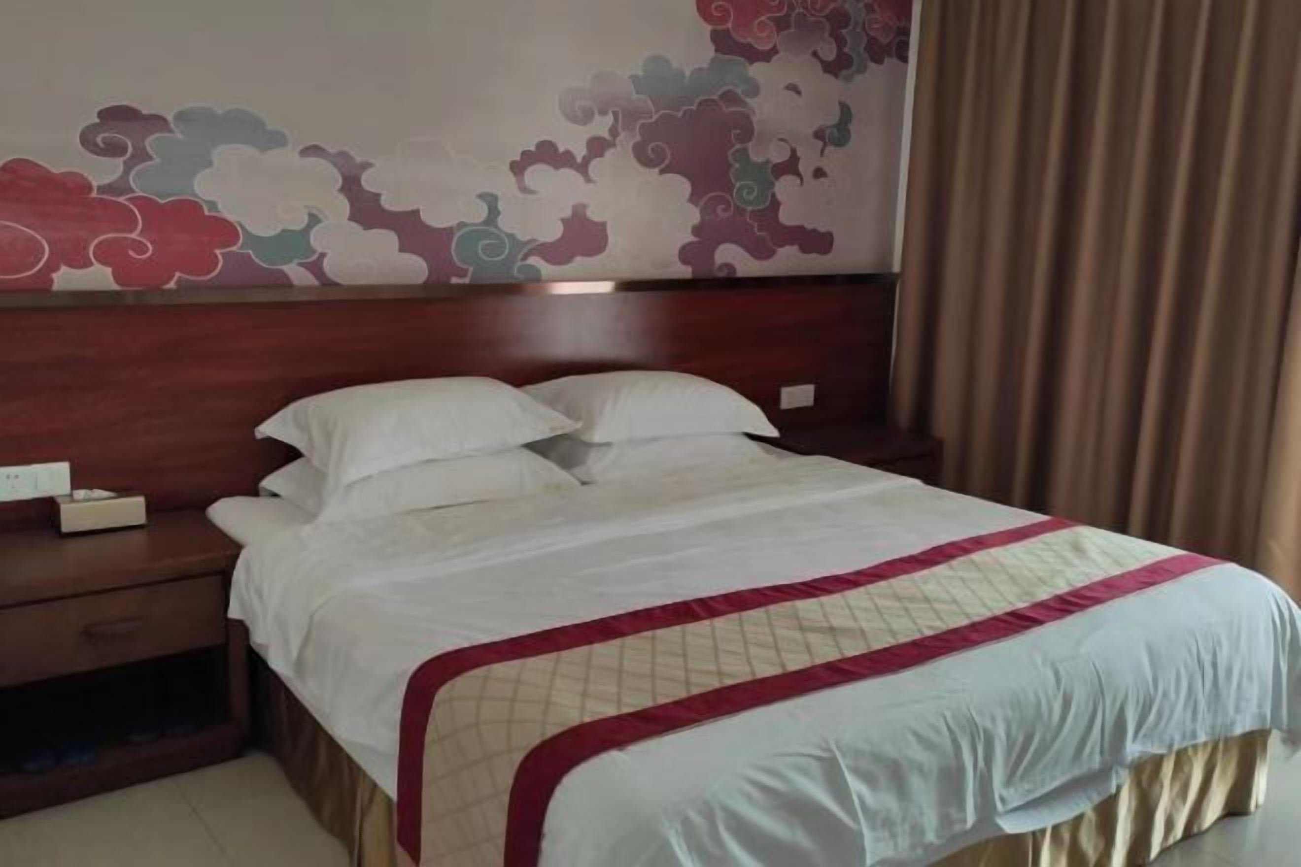 A neatly made bed with a white and red bedspread, a wooden headboard, and a wall with a cloud pattern.