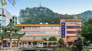 A hotel with a traditional Chinese architectural style, a large building with a blue sign, and a scenic view of a mountain in the background. - Qujiangying Hotel (Shaoguan)