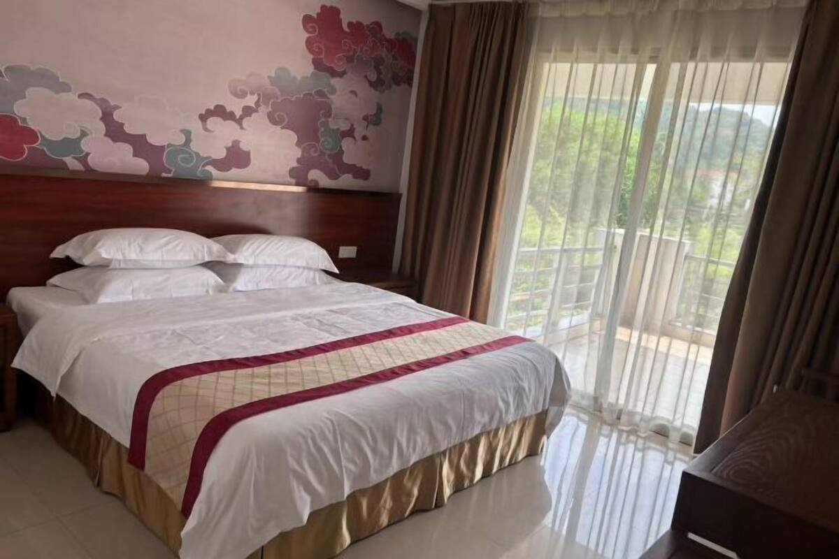 Ein Hotelzimmer mit einem großen Bett, einem hölzernen Kopfteil, Blick auf Grün durch das Fenster und einem dekorativen Wandbild.