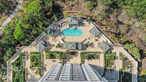 Une vue aérienne d’un complexe hôtelier doté d’une piscine centrale, de plusieurs espaces de détente et d’une disposition structurée avec des allées bien définies.