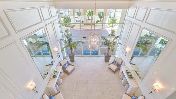 Un hall d’entrée spacieux avec un espace salon central, de grandes fenêtres et des plantes en pot.