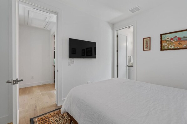 A bedroom with a bed, a television mounted on the wall, and a door leading to another room.