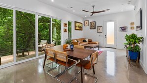 A spacious living area with a dining table, sofas, and a large sliding glass door leading to a deck. - Modern Treehouse Retreat, Cold Plunge (Austin)