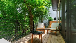 A wooden deck with two chairs and a small table, surrounded by lush green trees. - Modern Treehouse Retreat, Cold Plunge (Austin)