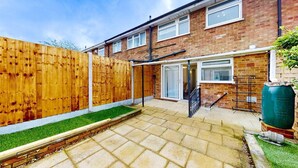 A residential backyard with a wooden fence, a paved patio, and a green lawn. - Ranworth House - Holiday Home in Bedford, Sleeps 5 (Bedford)