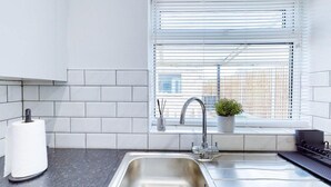 A modern kitchen with a stainless steel sink, white tiled backsplash, and a window with blinds. - Ranworth House - Holiday Home in Bedford, Sleeps 5 (Bedford)